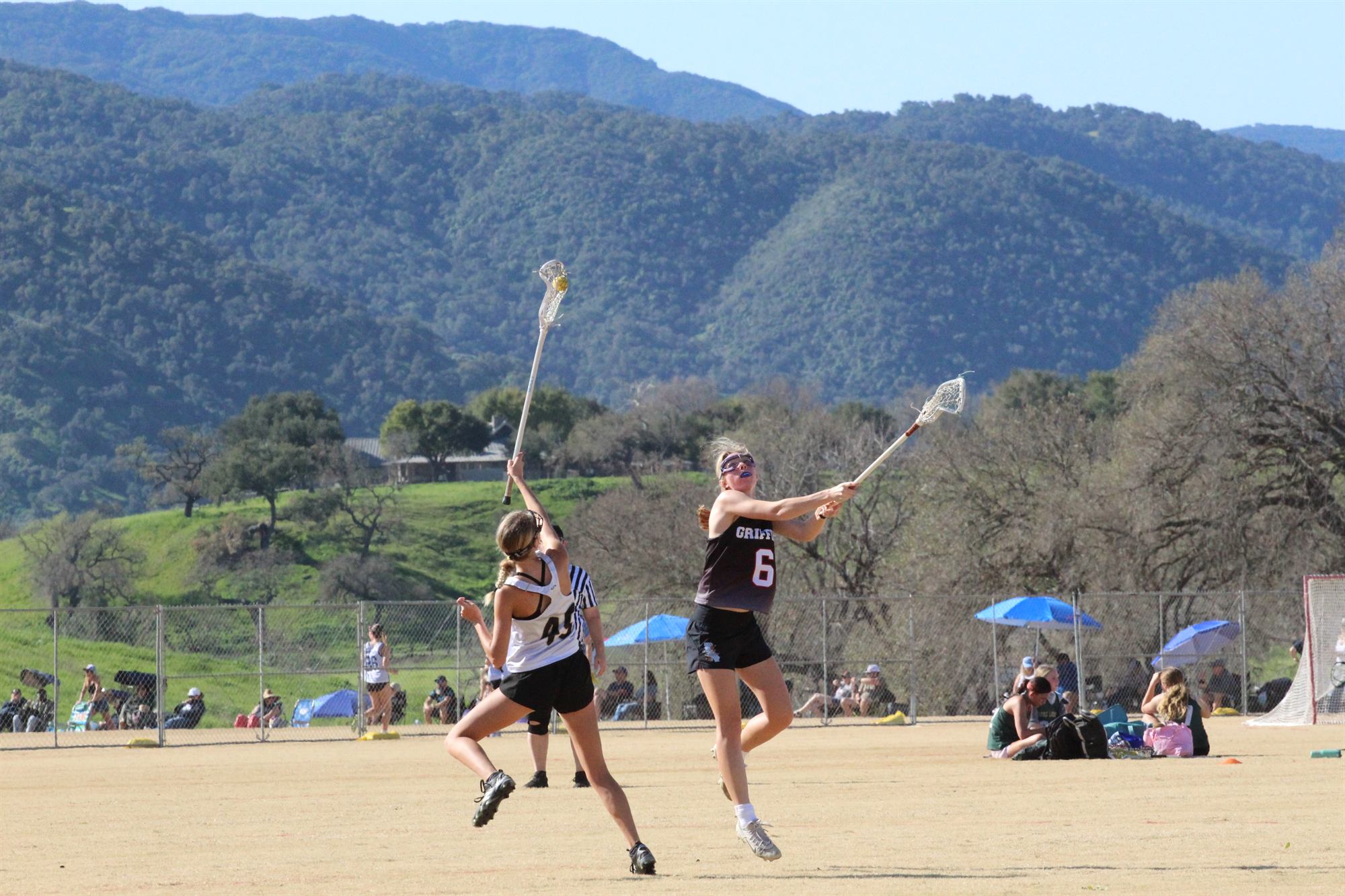 Two players leaping for the draw on an open field with the hills behind them.