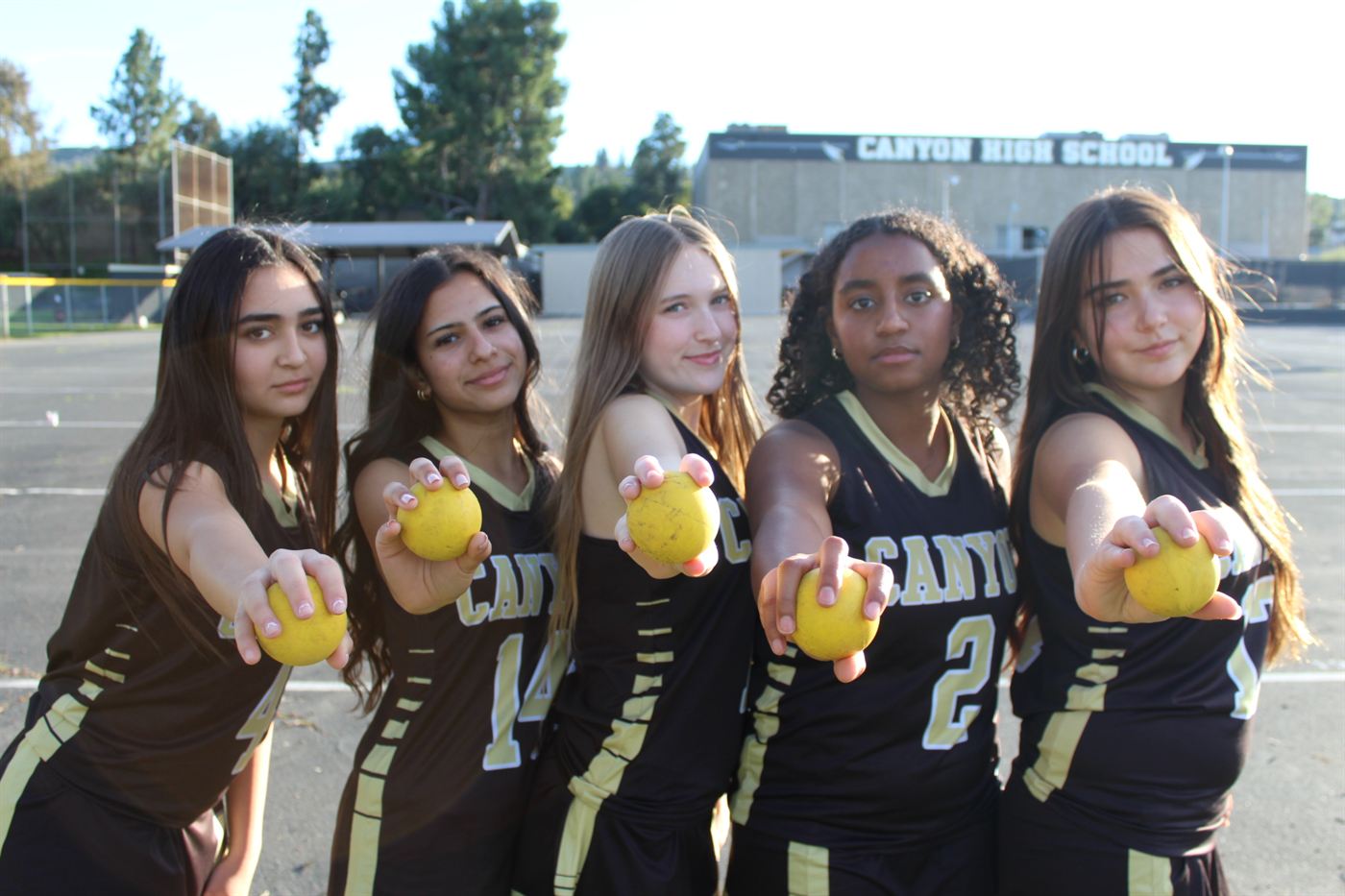 Five Canyon players holding lacrosse balls out toward the camera outside the school.